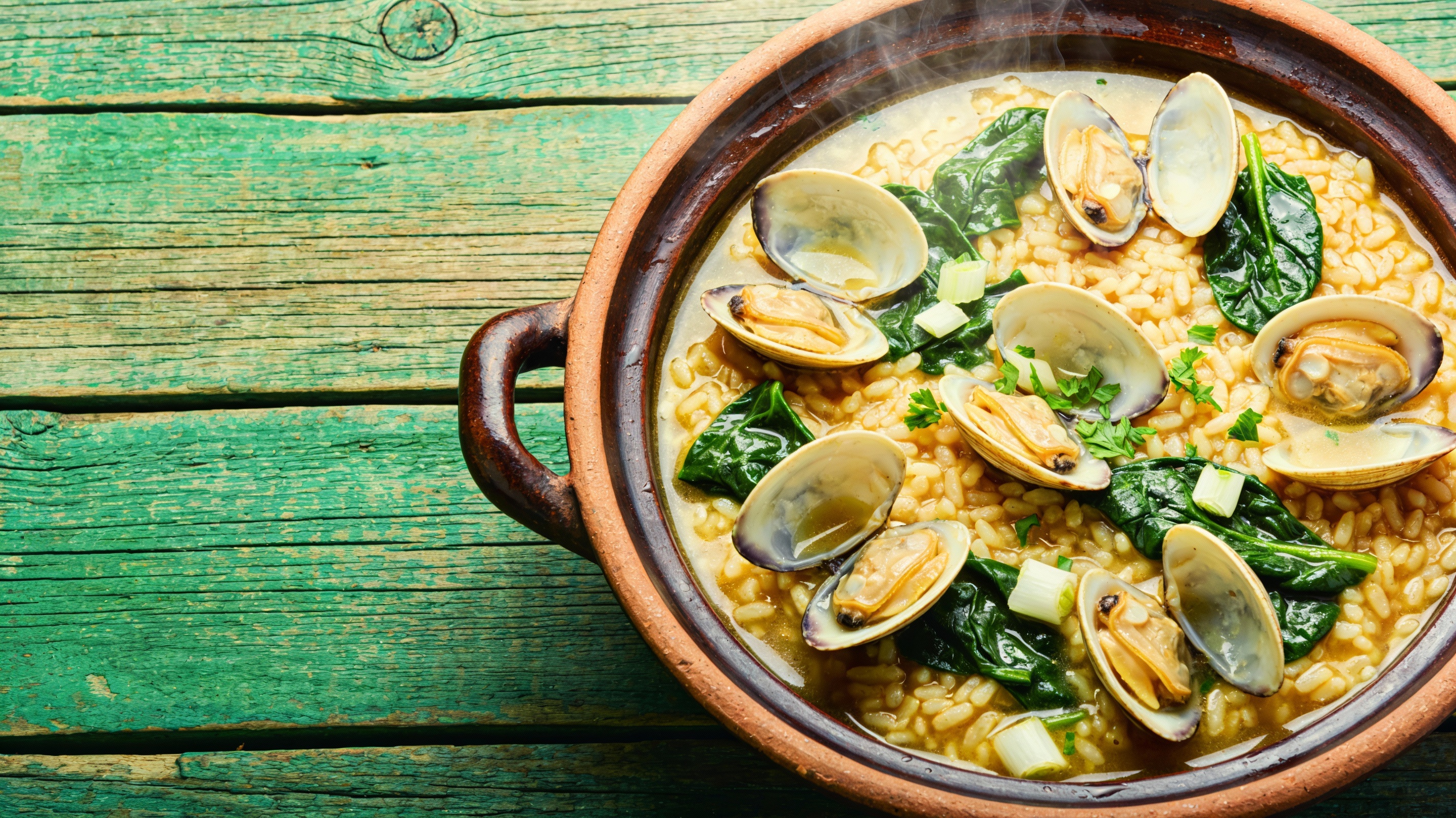 Arroz caldoso con almejas y espinacas frescas, servido en cazuela de barro